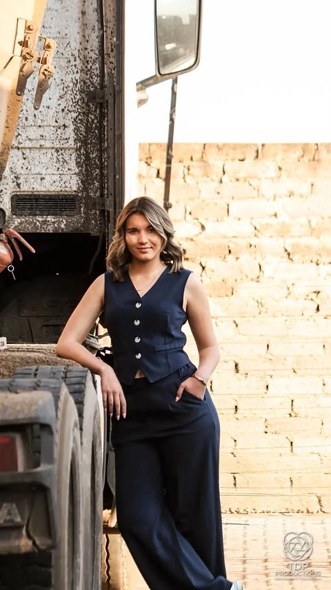 Woman in a navy waistcoat leaning against the side of a truck, one hand in her pocket