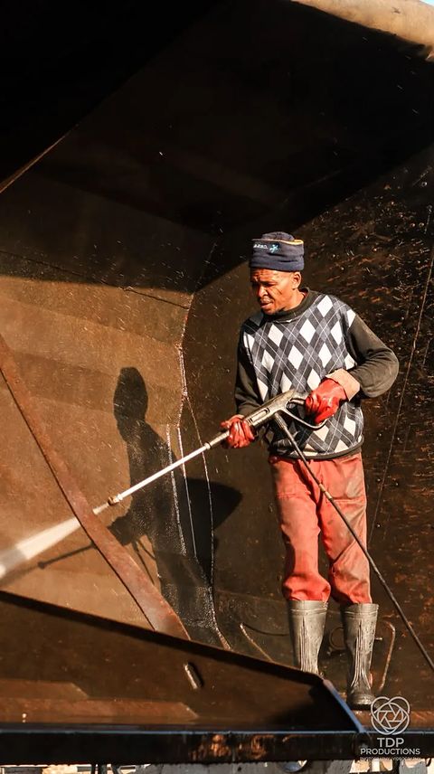 Worker in boots and red gloves pressure-washing the inside of a large tanker