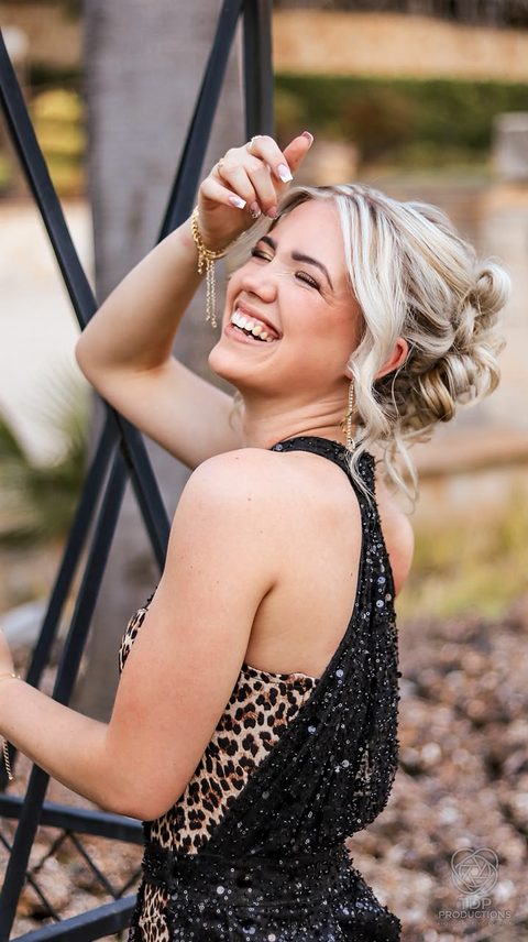 Young woman laughing in a black sequin and leopard-print gown, hand raised to her hair