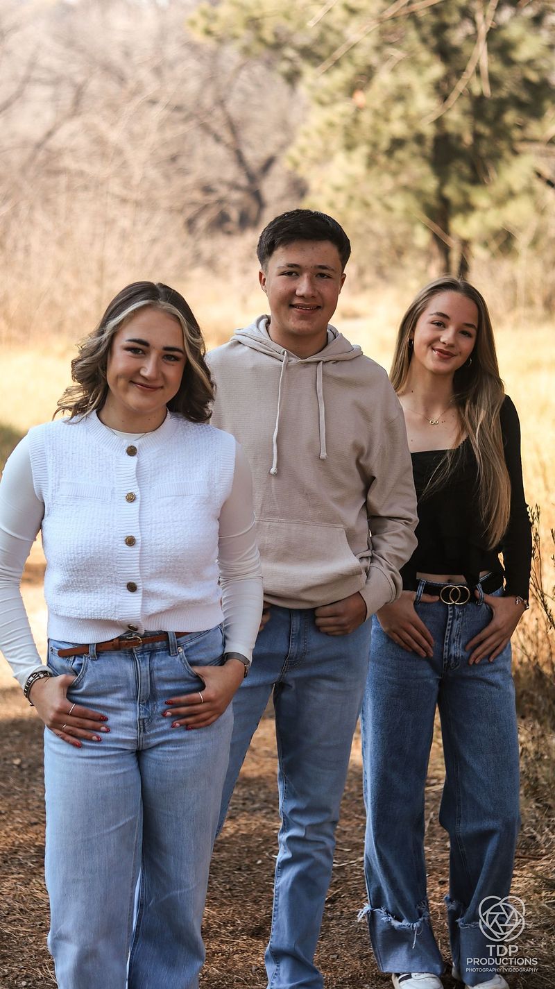 Three friends standing together in jeans and neutral tops on a wooded path